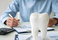 Man at desk calculating costs with calculator and paper with large model tooth