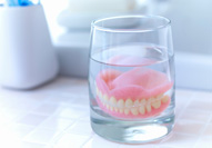 Full set of dentures in a glass of clear liquid on tiled countertop