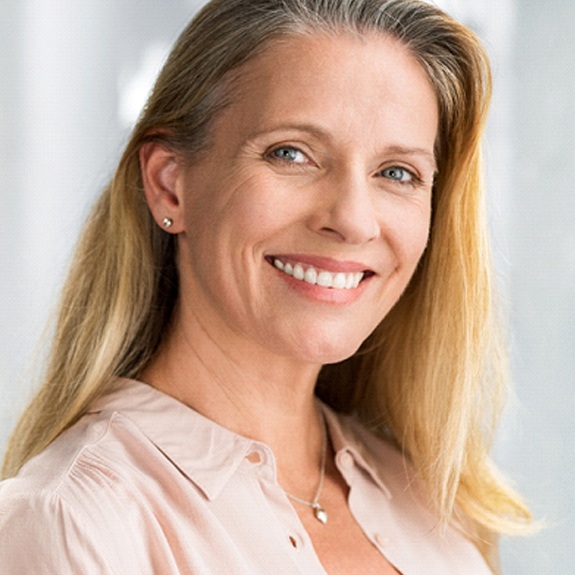 Senior woman in salmon-colored shirt smiling with dentures in Carmel, IN