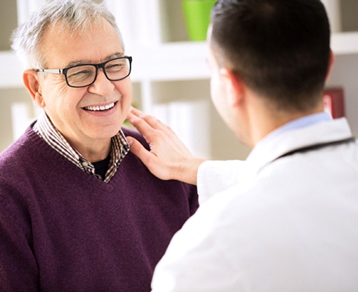 Older man smiling at dentist with hand on shoulder