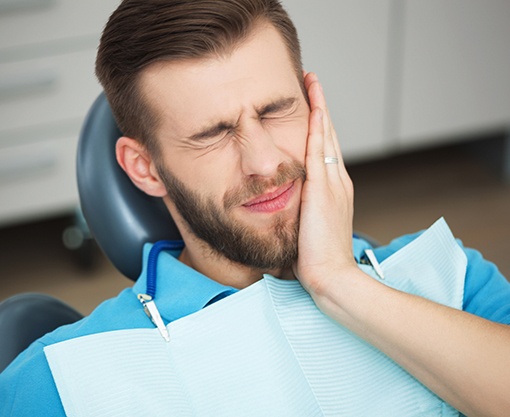 Man in dental chair holding cheek