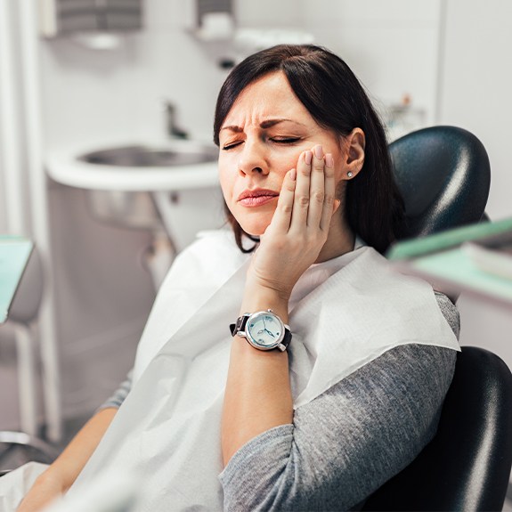 Woman in dental chair holding jaw