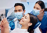 Patient admiring the results of her treatment with mirror next to 2 dentists