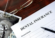  Top corner of dental insurance form on desk next to x-ray image, pen, and glasses