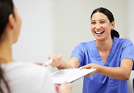 Woman in blue scrubs handing paperwork on clipboard to patients