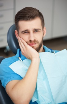 Man in dental chair holding his jaw in pain