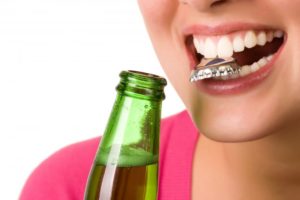 woman using her dental implants to open a glass bottle of soda 