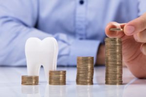 Model tooth and stacks of coins representing cost of dental implants