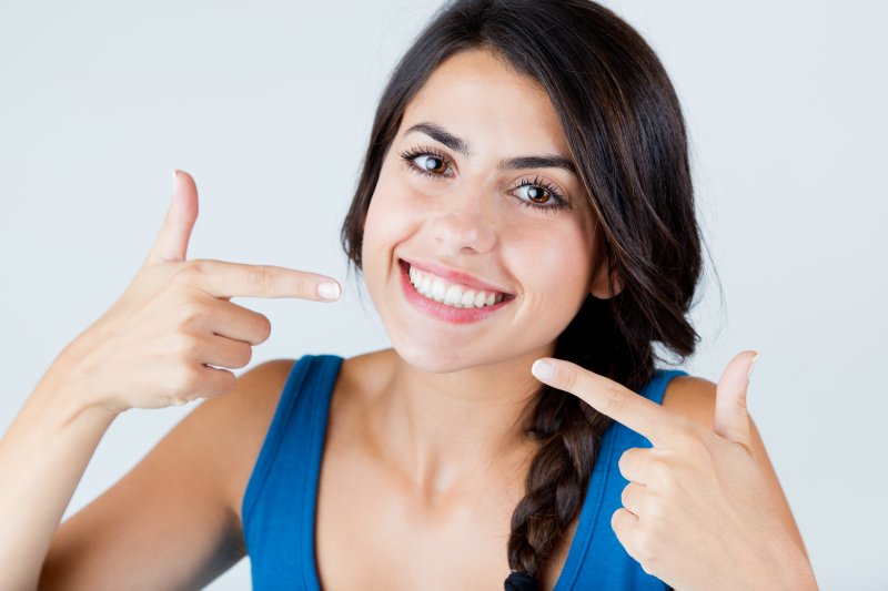 young woman smiling and pointing to her white teeth