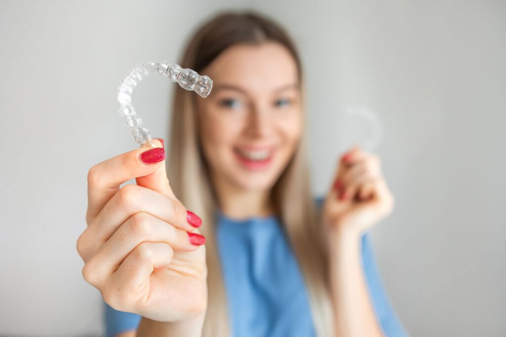 Woman in blue shirt with red nails holding Invisalign trays