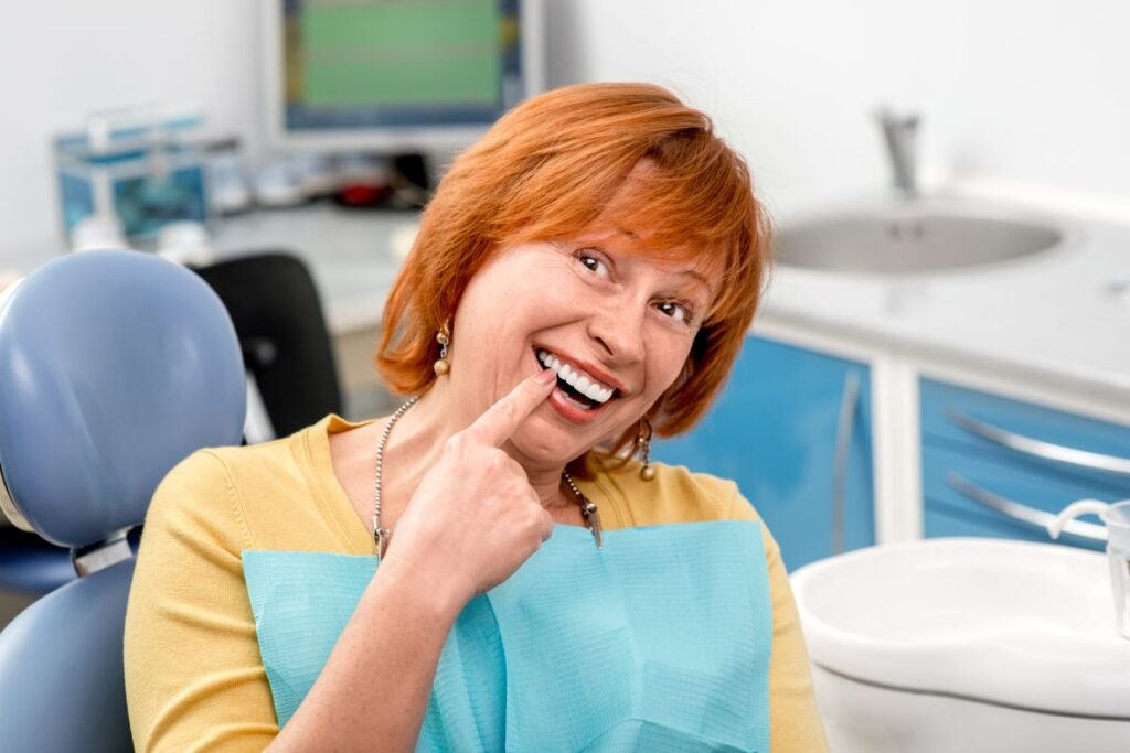 A woman in a dental chair pointing to her dental implant